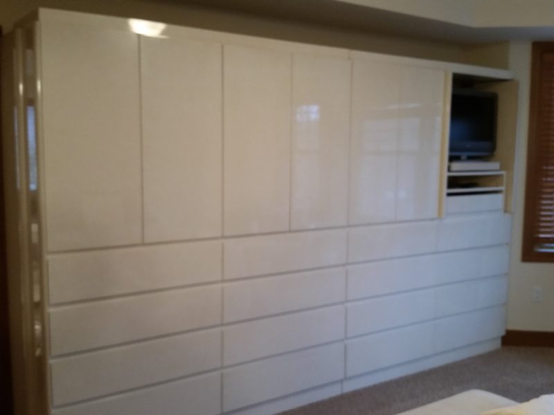 Angled view of glossy white wall cabinetry with rows of drawers and a TV niche