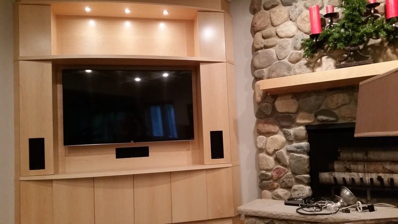 Light wood media wall with a mounted TV beside a stone fireplace