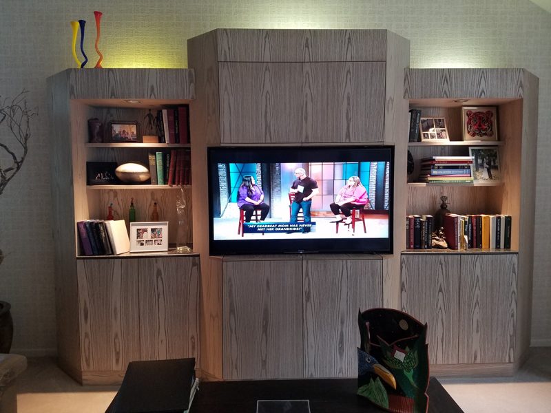 Gray wood-grain media wall with lit bookshelves flanking a mounted TV