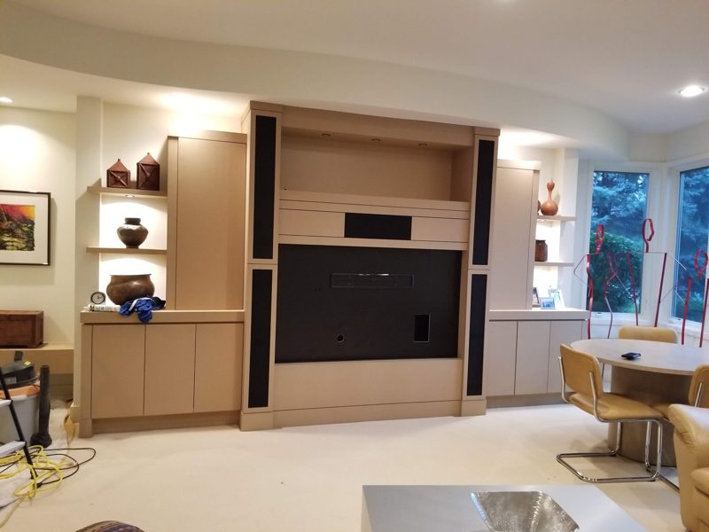 Light wood media wall with a TV opening, speakers, and lit side niches