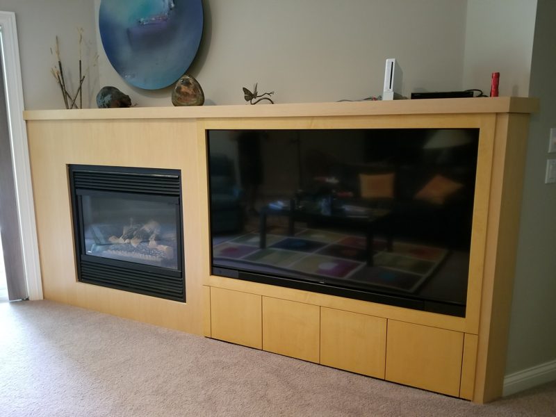 Light wood surround framing a gas fireplace and a wide TV screen