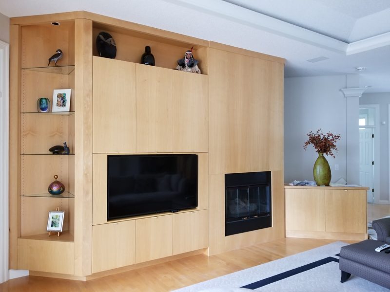 Light wood media wall with a TV, fireplace, and glass display shelves