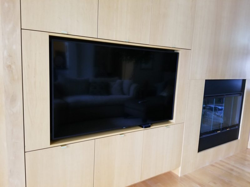 Close view of a large TV set into light wood paneling beside a fireplace