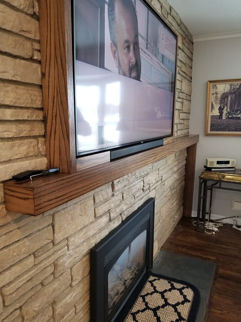Stacked stone fireplace with a wood mantel and a TV mounted above
