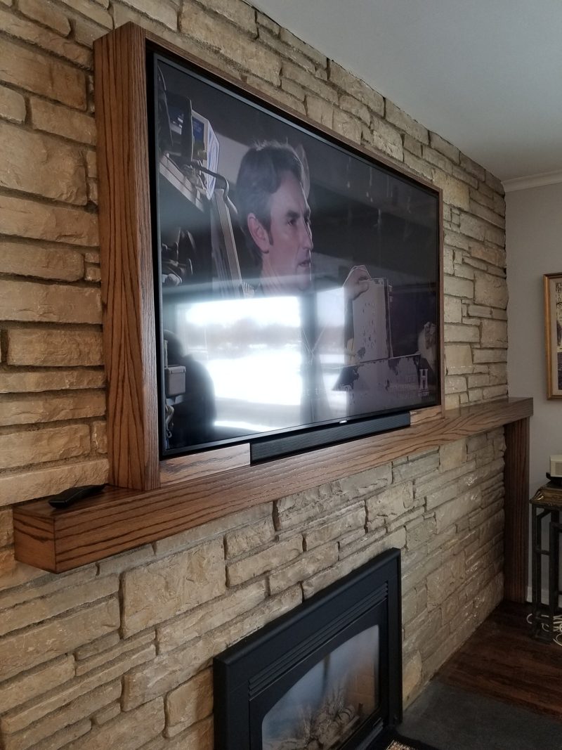 Angled view of a wood-framed TV above a stone fireplace and mantel