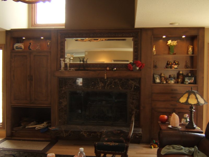 Dark wood built-ins with cabinets and lit shelves around a fireplace