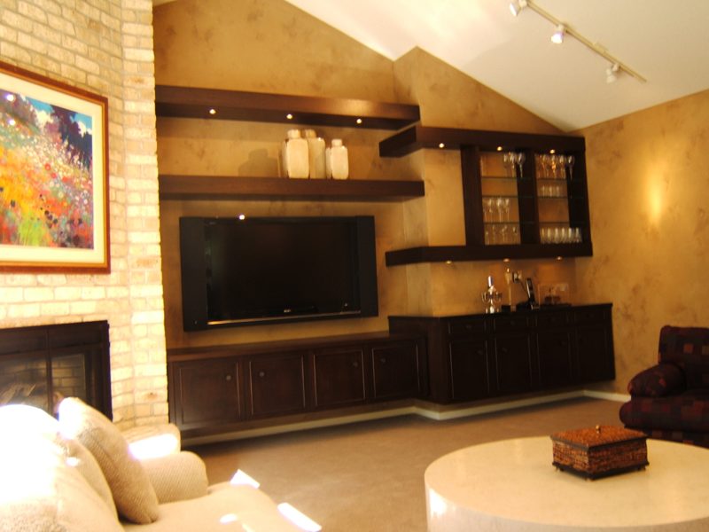 Dark wood floating shelves and low cabinets around a wall-mounted TV