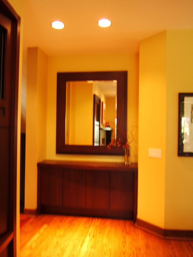 Dark wood wall cabinet below a framed mirror in a warm-toned alcove
