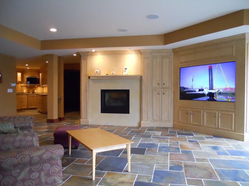 Wider view of cream built-ins around a fireplace and TV over a slate floor