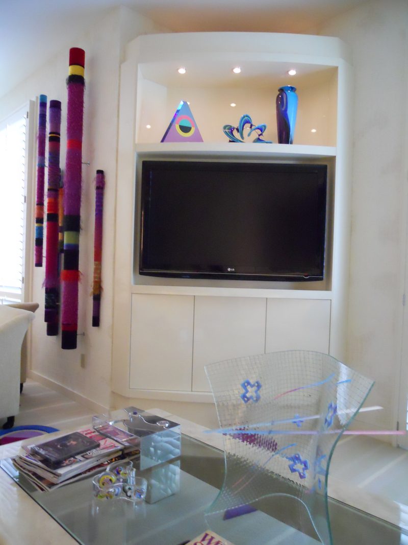 White built-in niche with a TV, a lit upper shelf, and colorful art