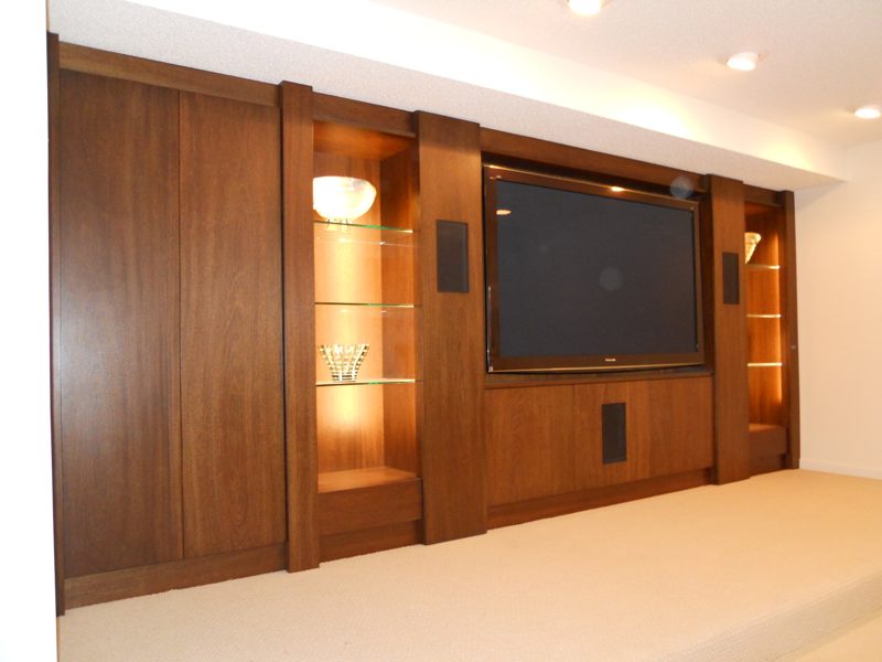 Dark wood media wall with lit glass display niches and a large TV