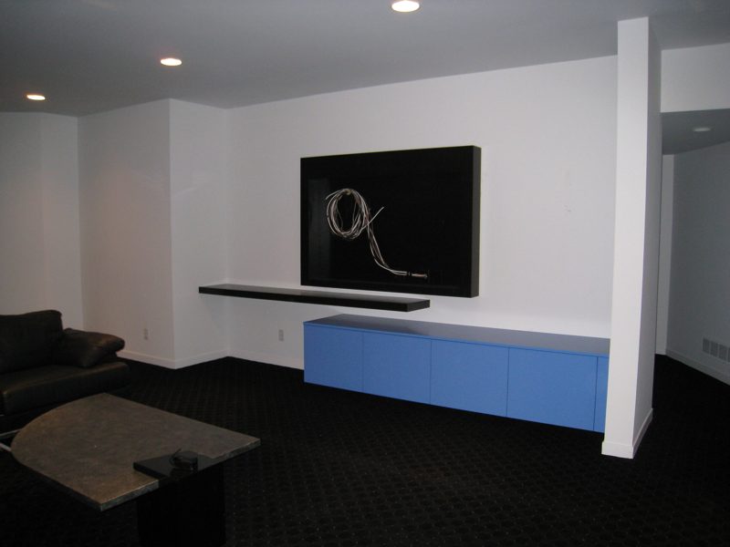 Floating blue cabinets below a dark shelf and a wall-mounted TV