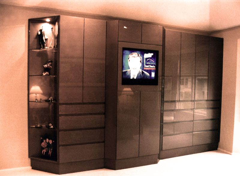 Dark wood wall of cabinets and drawers with display shelves and a TV