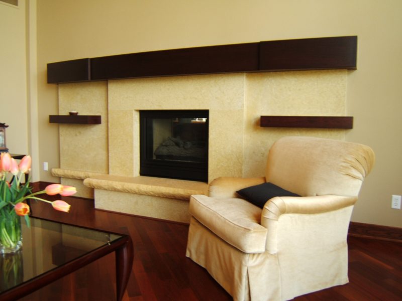 Dark wood floating shelves above a fireplace beside a cream armchair
