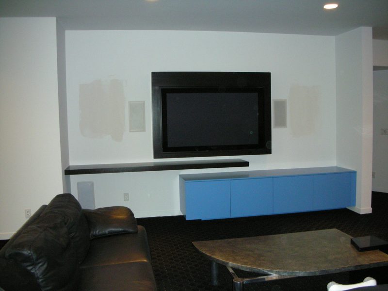 Wall-mounted TV above a floating blue cabinet and a dark shelf