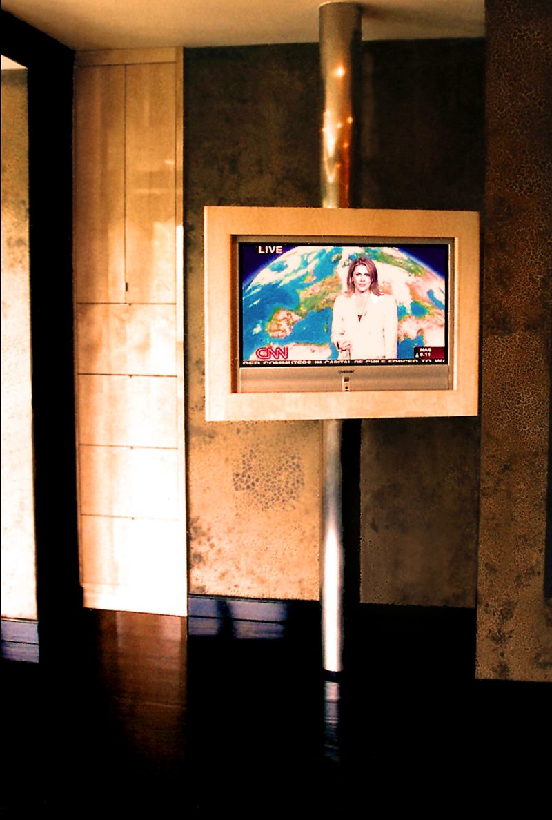 Framed TV mounted on a metal pole against warm textured wall panels