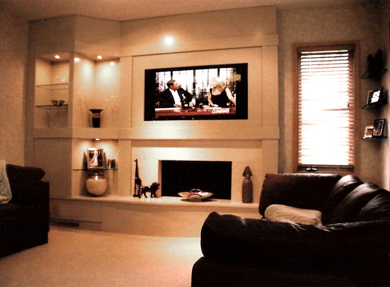Cream media wall with a TV above a fireplace and lit corner shelves