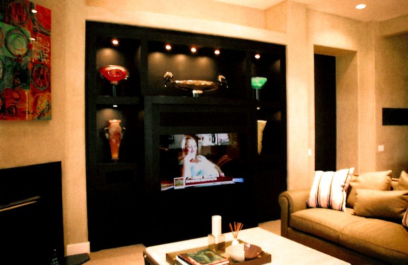 Black built-in wall with a TV and lit display niches in a living room