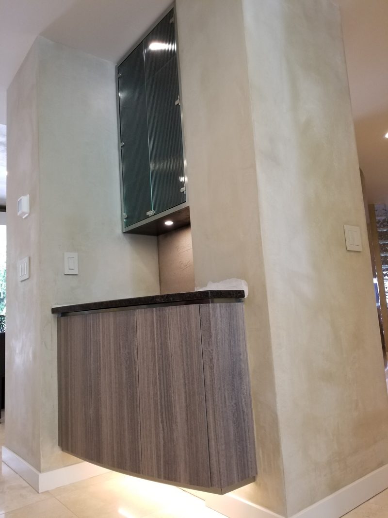 Angled view of a floating gray cabinet and glass upper in a plaster column