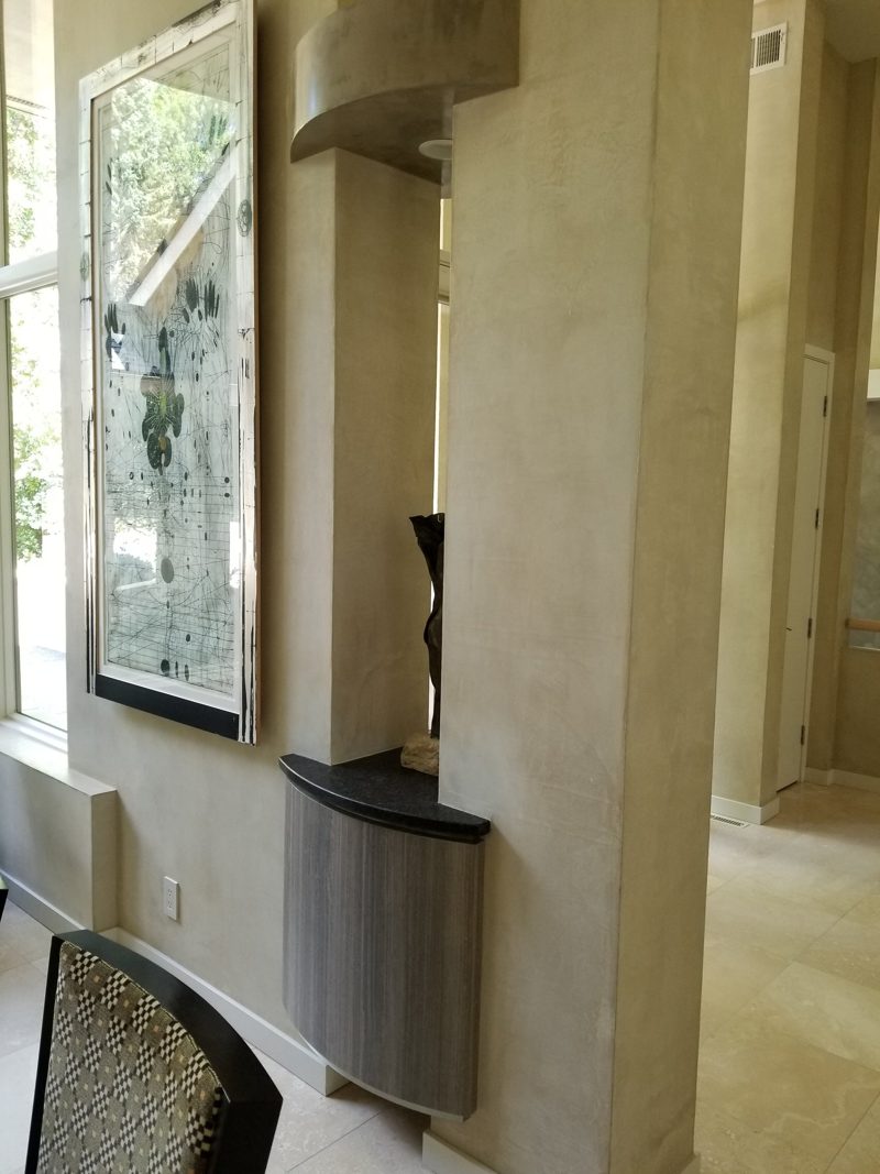 Curved floating gray cabinet with a dark top beside a tall column