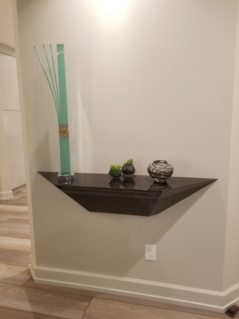 Floating dark wedge-shaped wall shelf holding small decor