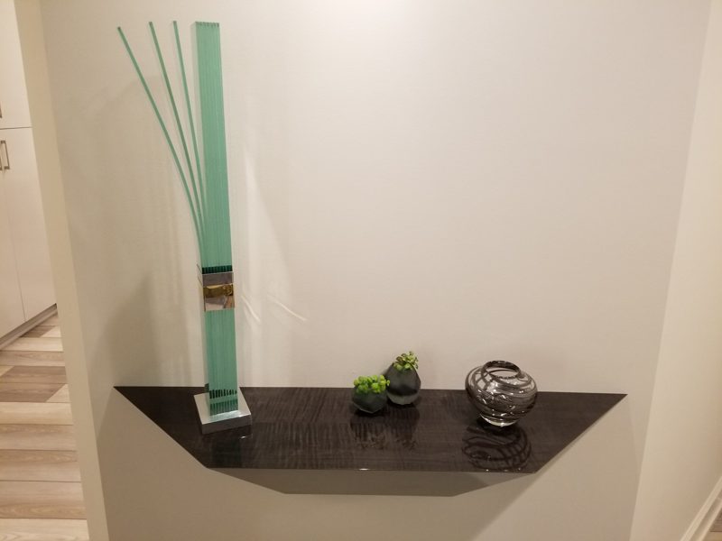Close view of a dark tapered floating shelf with a tall glass vase