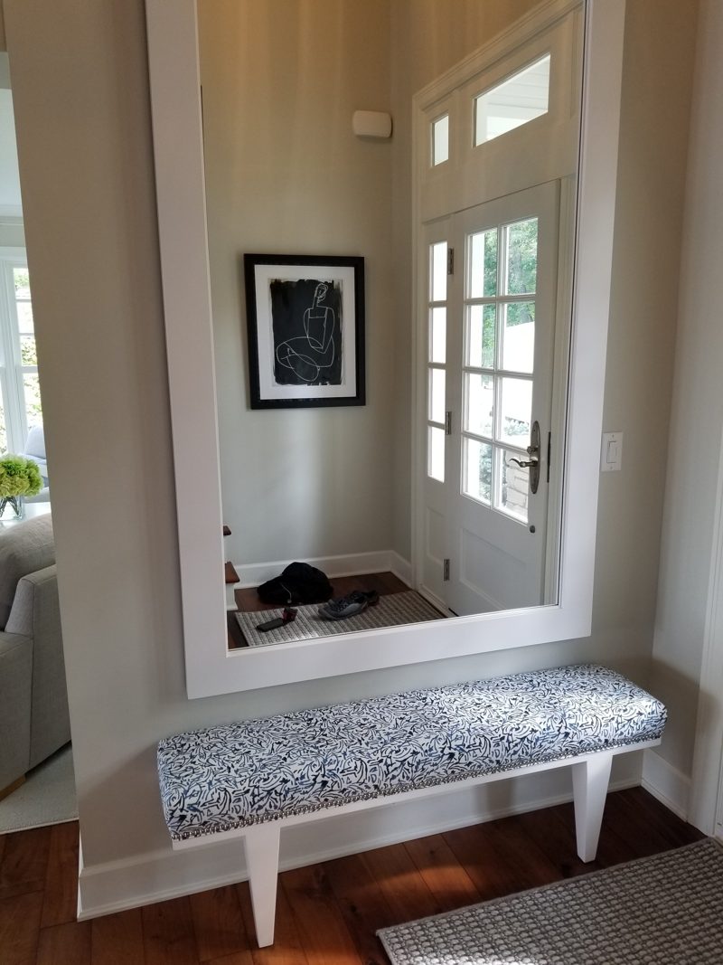 Upholstered entry bench with white legs below a large mirror