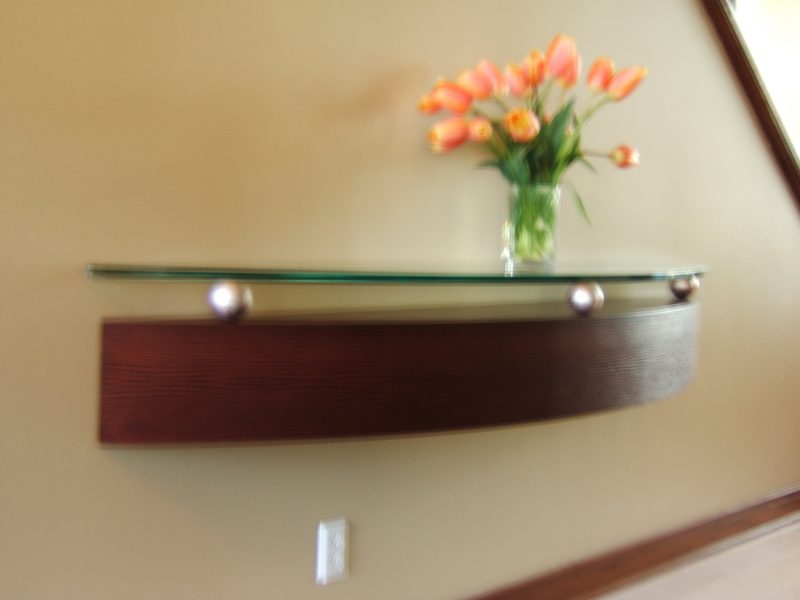 Curved dark wood wall shelf with a glass top and flowers