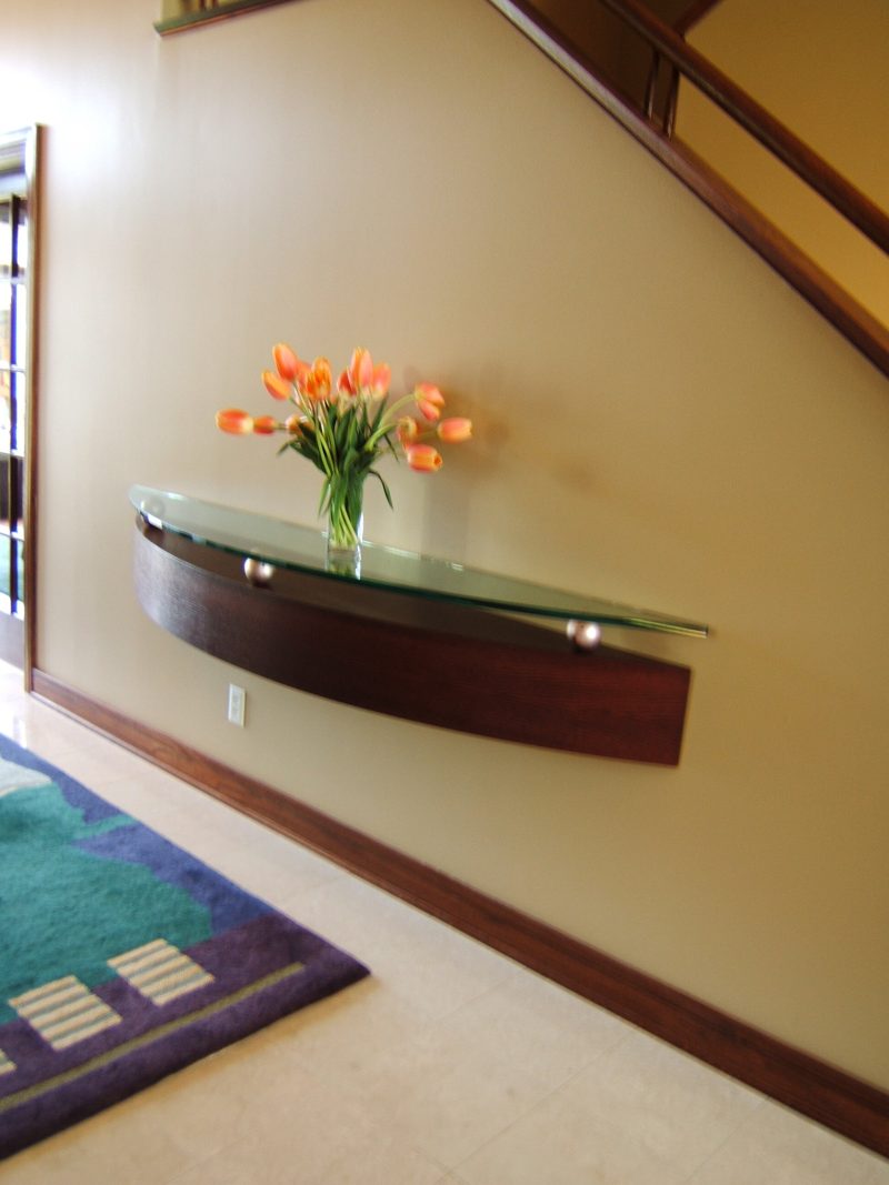 Angled view of a curved wood and glass wall shelf below a staircase