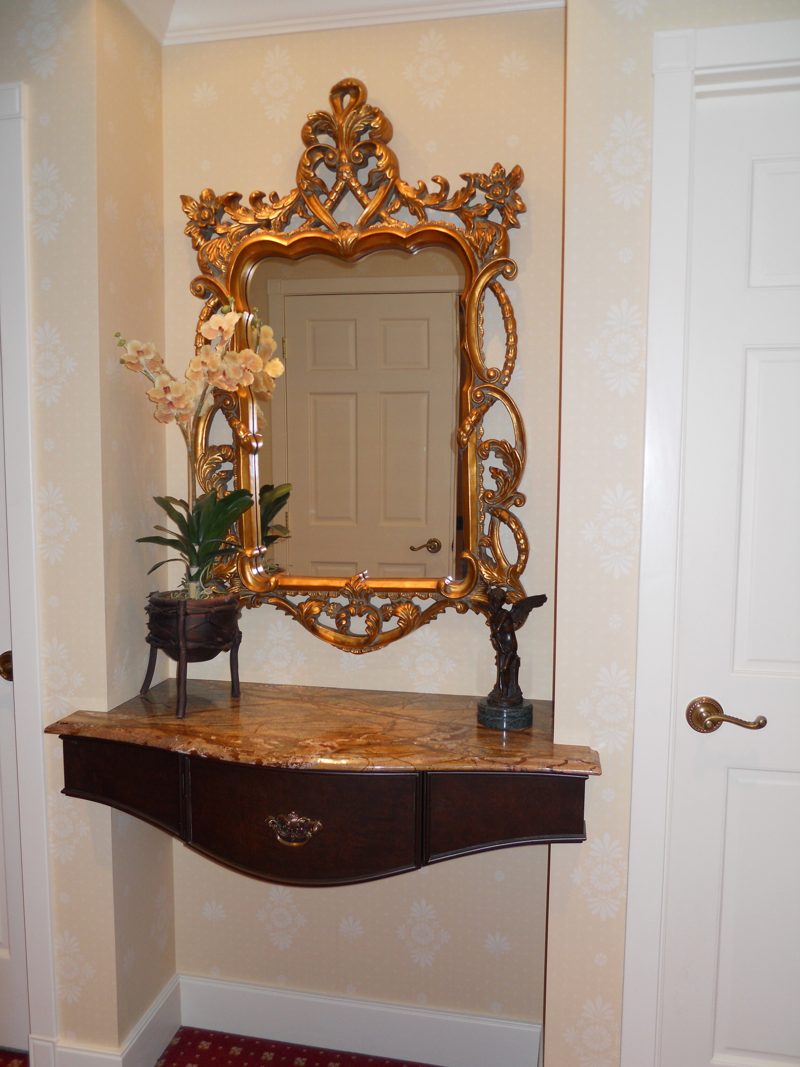 Wall-mounted curved console with a stone top below an ornate gilt mirror
