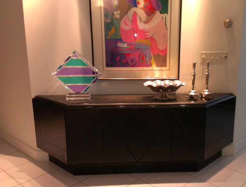 Glossy black angled sideboard below colorful framed artwork