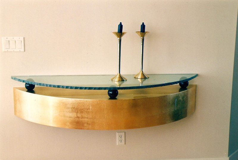 Gold-leaf curved wall shelf with a glass top and candlesticks