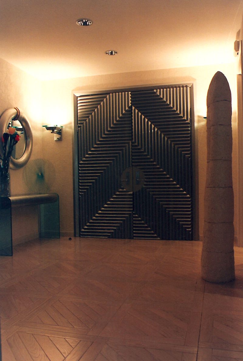 Chevron-pattern double doors in a warmly lit foyer with a tall sculpture