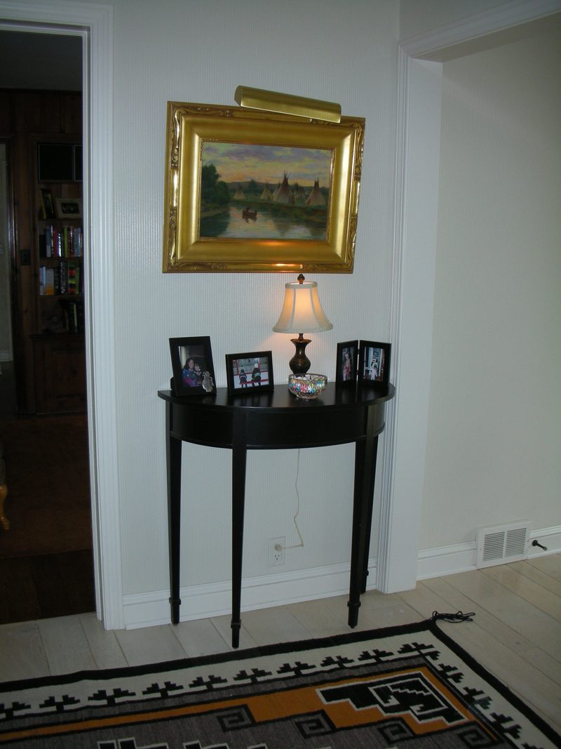 Black demilune hall table below a framed landscape painting