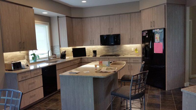 Kitchen with light oak-grain cabinetry, an island with stools, and a black refrigerator