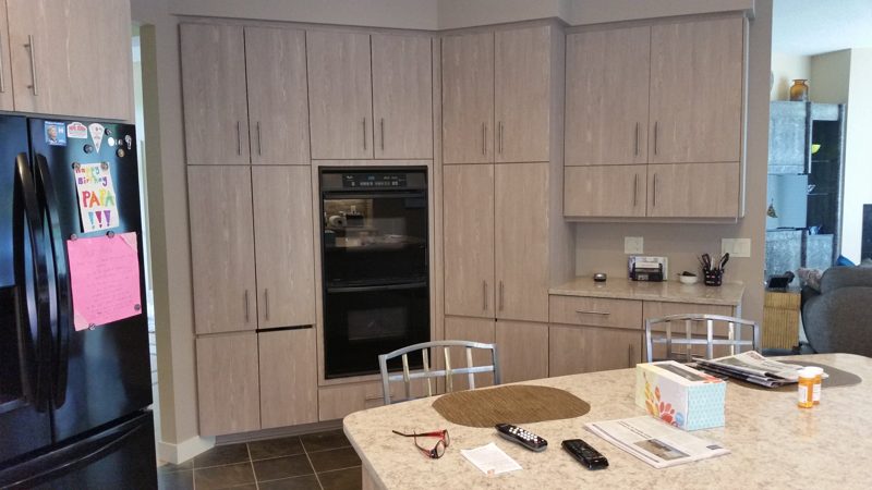 Wall of light oak-grain cabinets with built-in ovens beside a black refrigerator