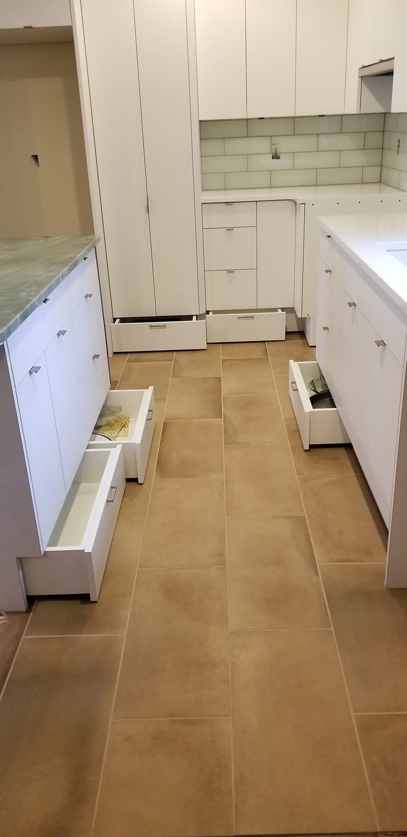 Galley of white cabinetry with open drawers and a tile backsplash