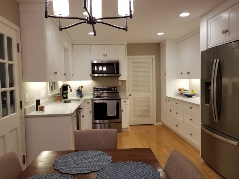 White kitchen with a glass-front corner cabinet and stainless appliances beside a dining table