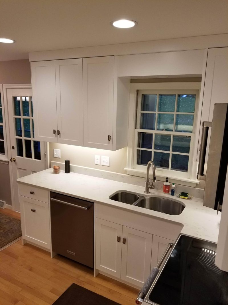 White kitchen sink wall with a window, dishwasher, and wood floor
