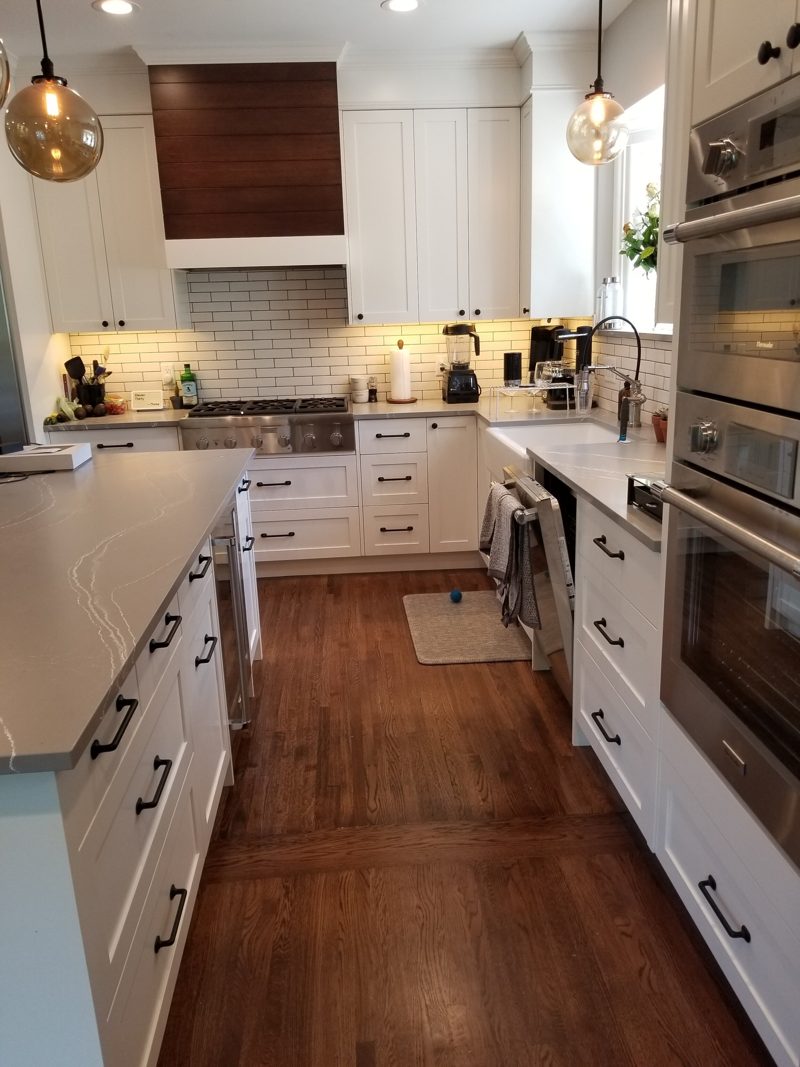 White galley kitchen with a wood range hood, wall ovens, and pendant lights