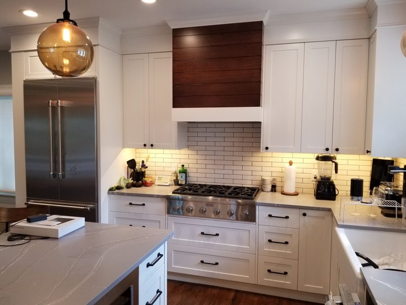 White kitchen with a walnut range hood, subway tile, and stainless refrigerator