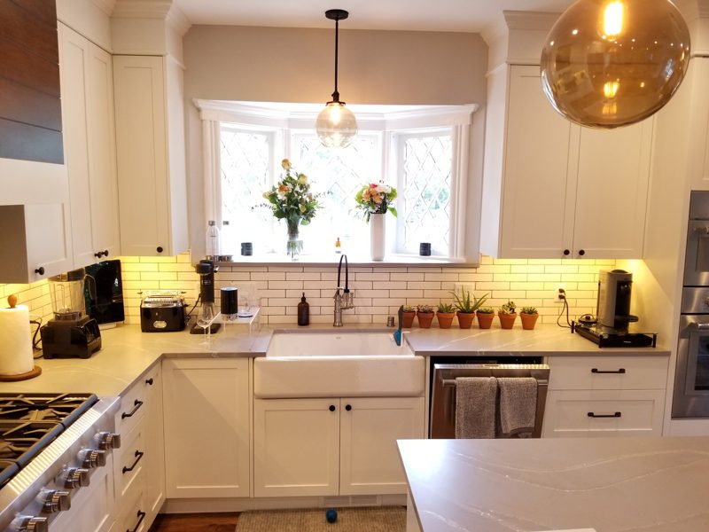 White kitchen with a farmhouse sink below a bay window and glass pendant lights