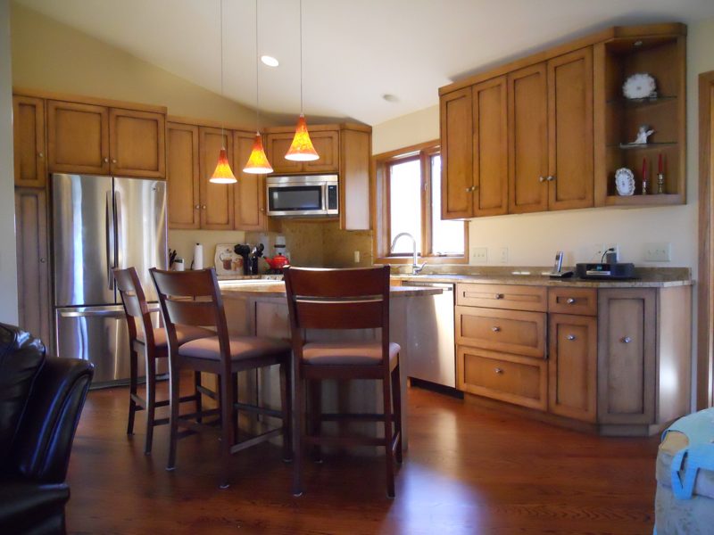 Oak cabinetry under a vaulted ceiling with a raised island and tall dining chairs