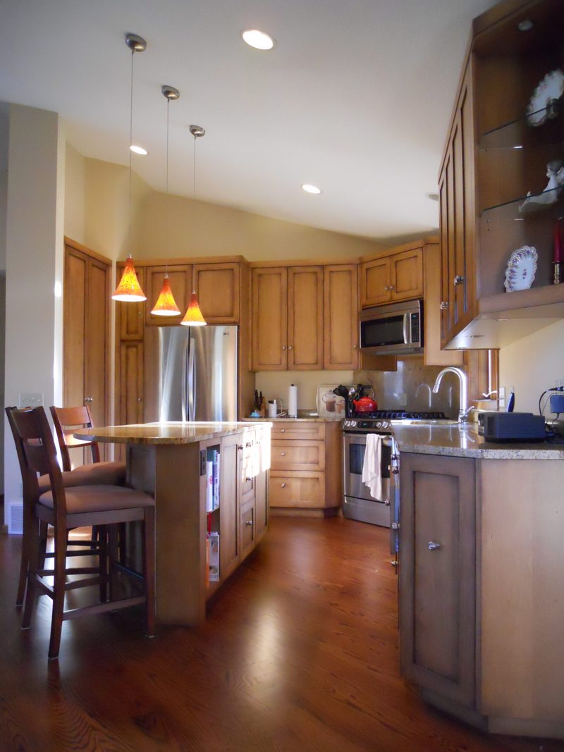 Oak kitchen with pendant lights over an island, seen from the dining area