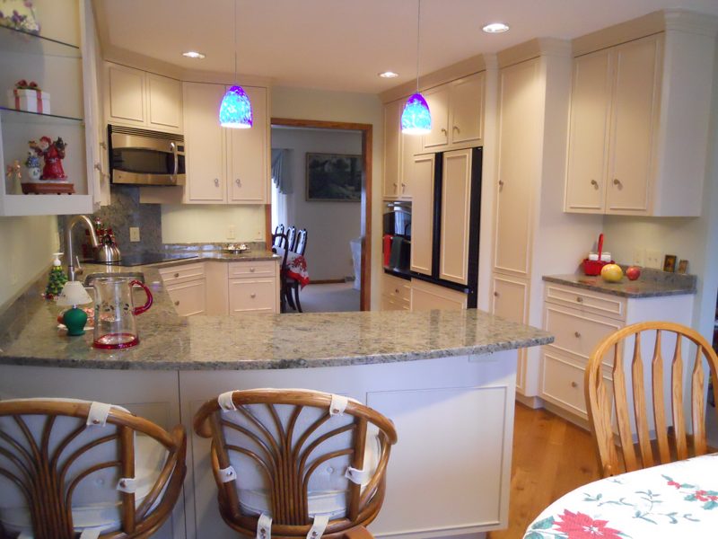 Cream cabinetry with a granite peninsula and blue glass pendants
