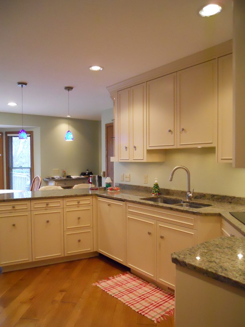 Cream cabinets around a corner sink with granite counters and a wood floor