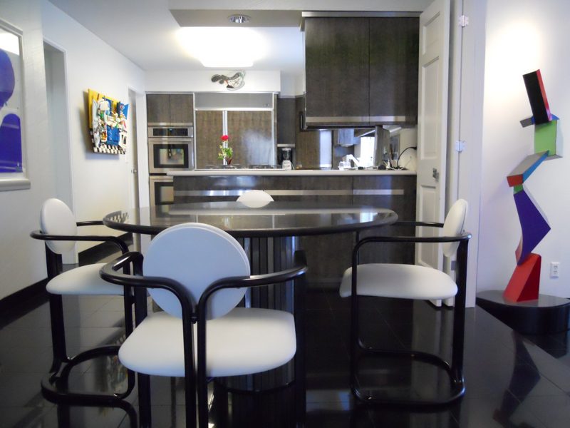 Modern kitchen with black cabinetry, white bar stools, and colorful artwork