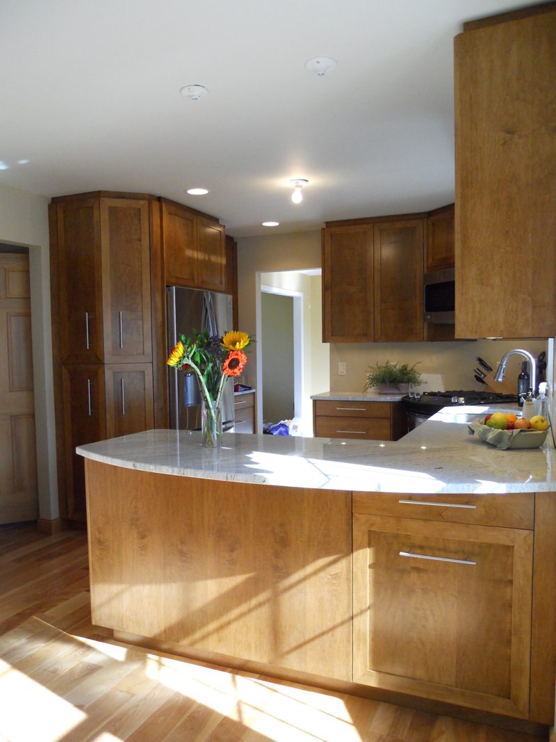 Wood island with a curved white counter and flowers, with cabinets beyond