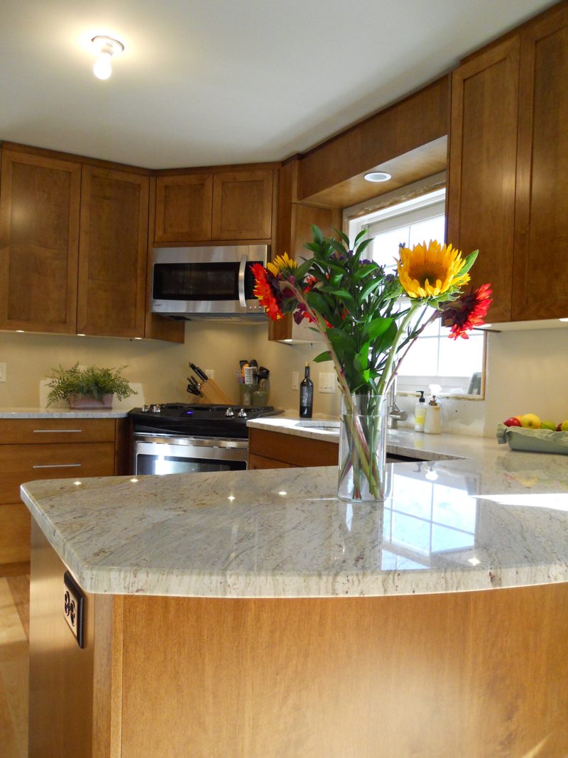 Curved island with a white counter and sunflowers in front of wood cabinets