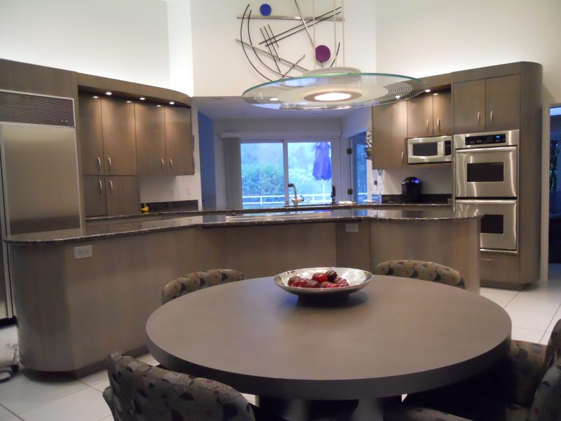 Round table in front of a taupe kitchen with a sculptural ceiling light
